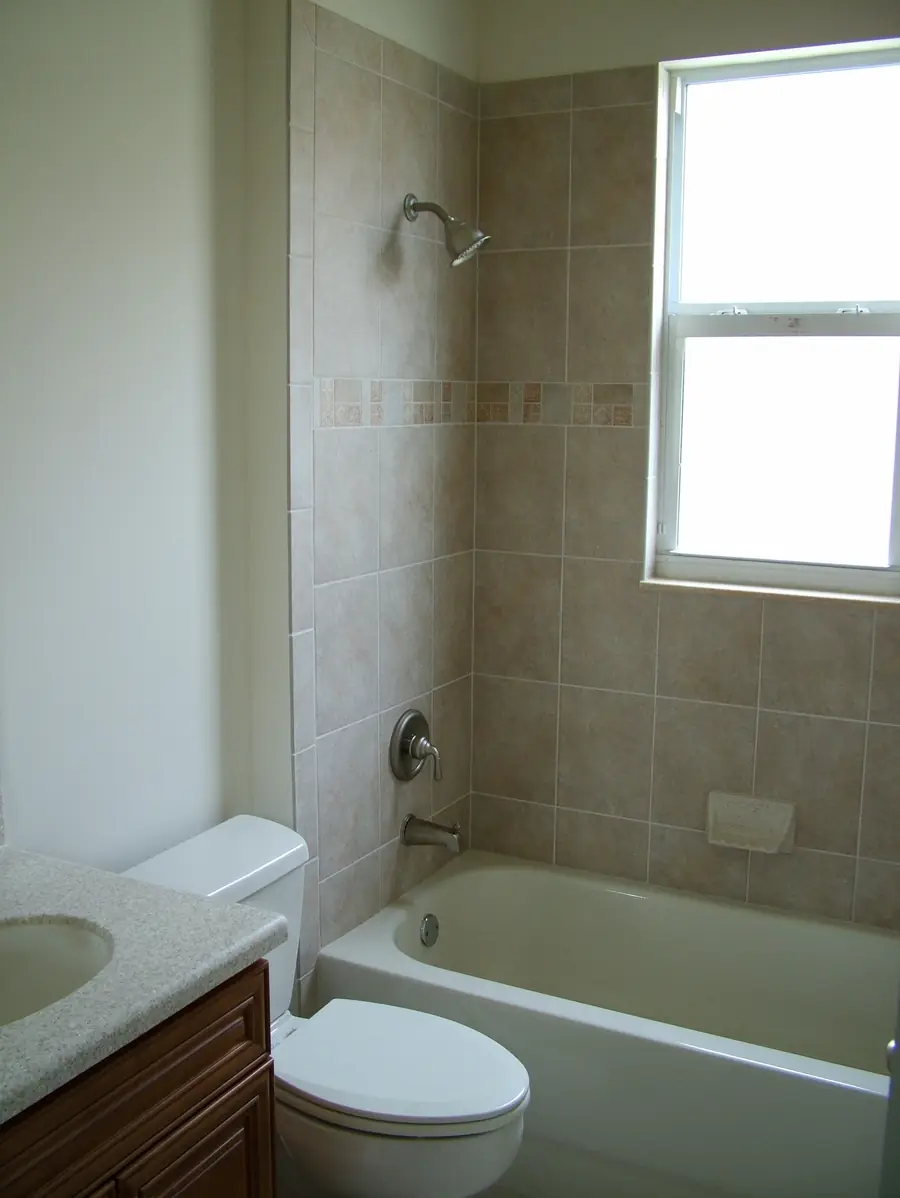 A finished bathroom: a tub and shower with the valve, spout and showerhead set in beige tile, beside a toilet and vanity
